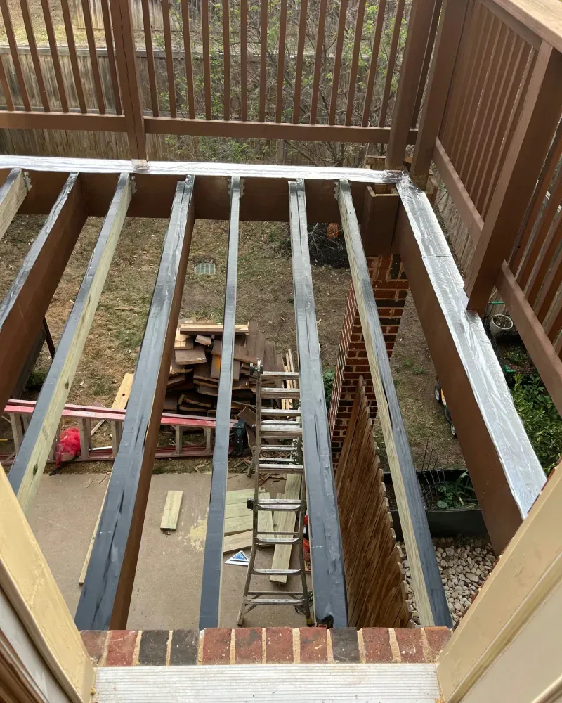 View from a doorway onto a partially constructed deck; wooden frame with visible joists, stairs below.