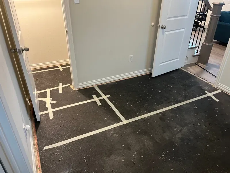 Room with dark floor marked with white tape. Doors and a staircase are visible.