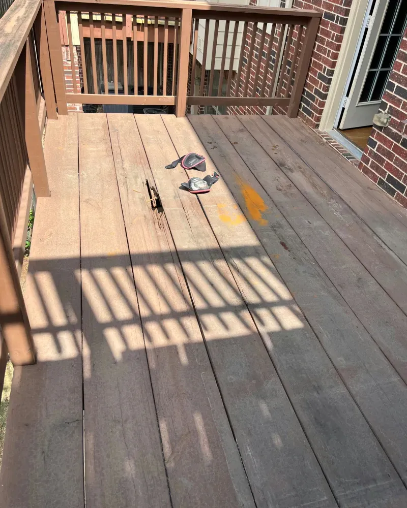 Wooden deck with railings. Sunlight casts long shadows. Some items and a yellow marking are on the deck.