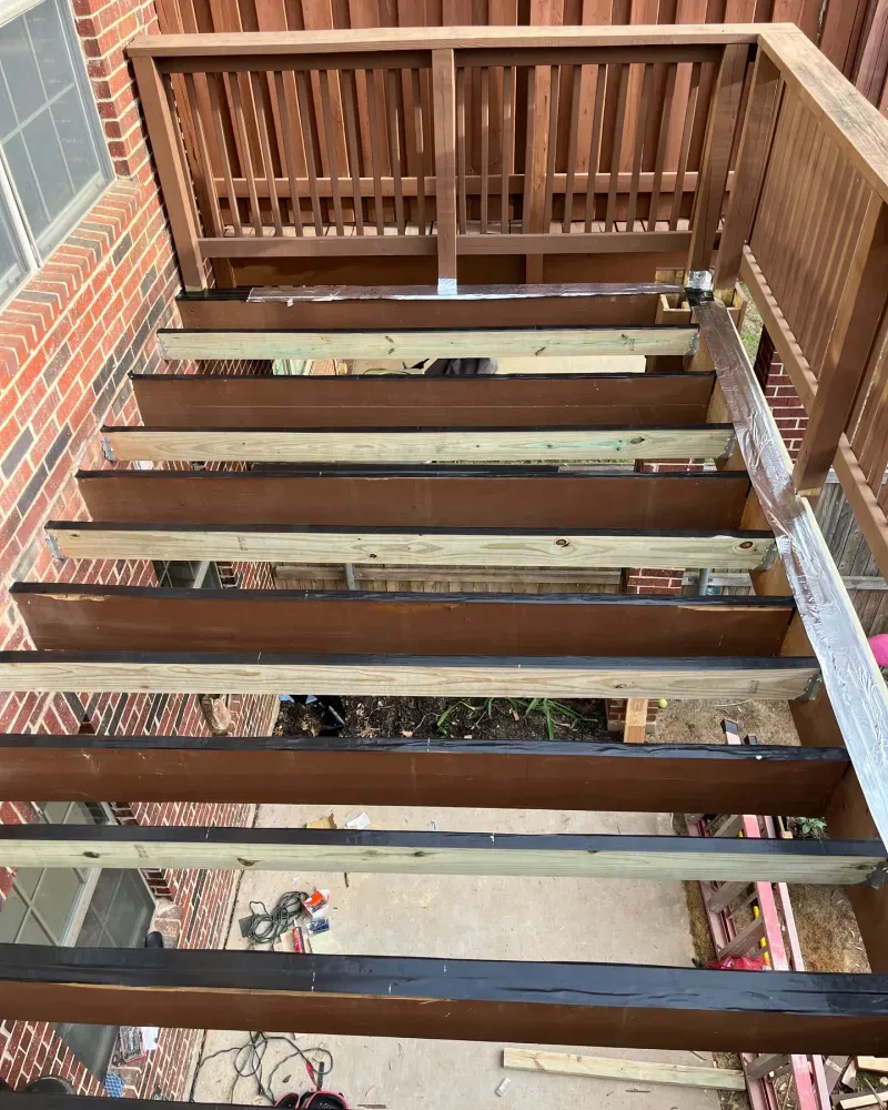 Wooden outdoor staircase under construction; brown and light wood planks, leading to a deck.