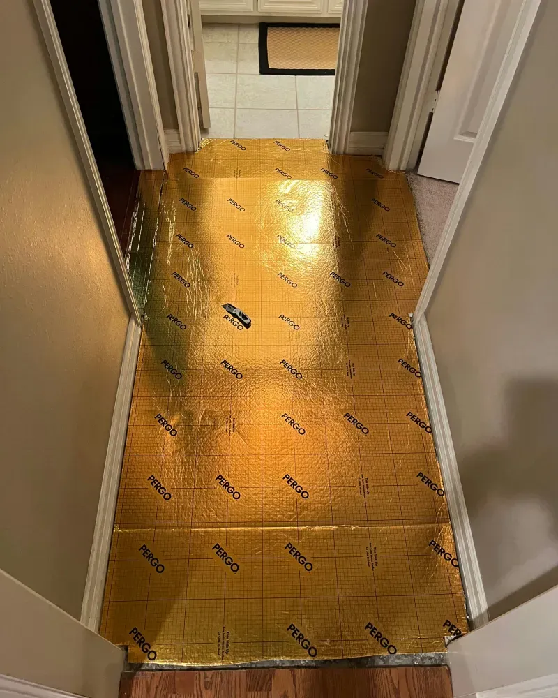 Gold underlayment installed in a hallway, ready for flooring. Hallway is between two doorways.