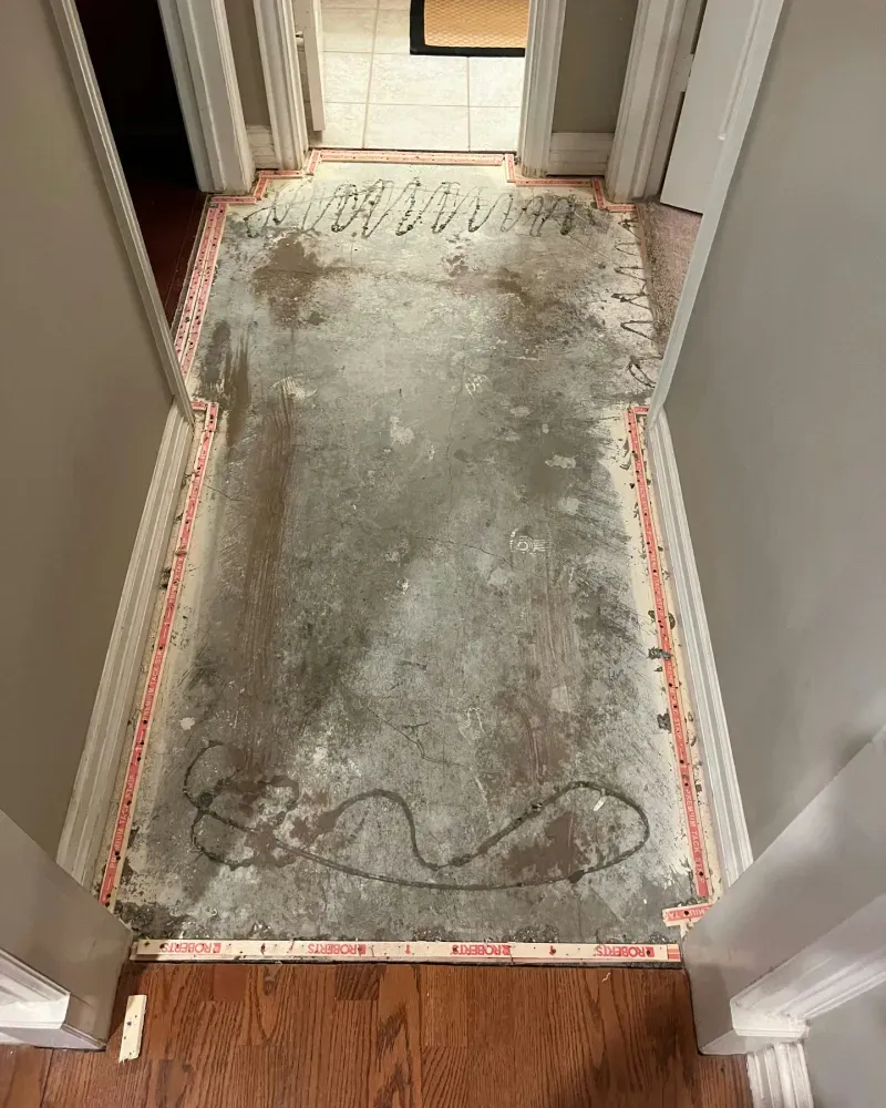 Hallway with carpet removed, showing concrete floor and tack strips along the edges.