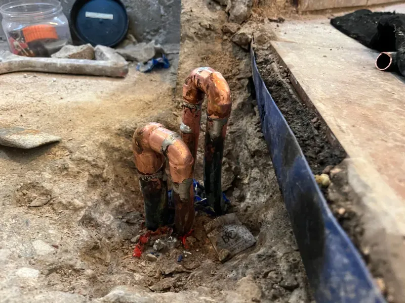 Copper pipes exposed in a trench, likely during plumbing work.