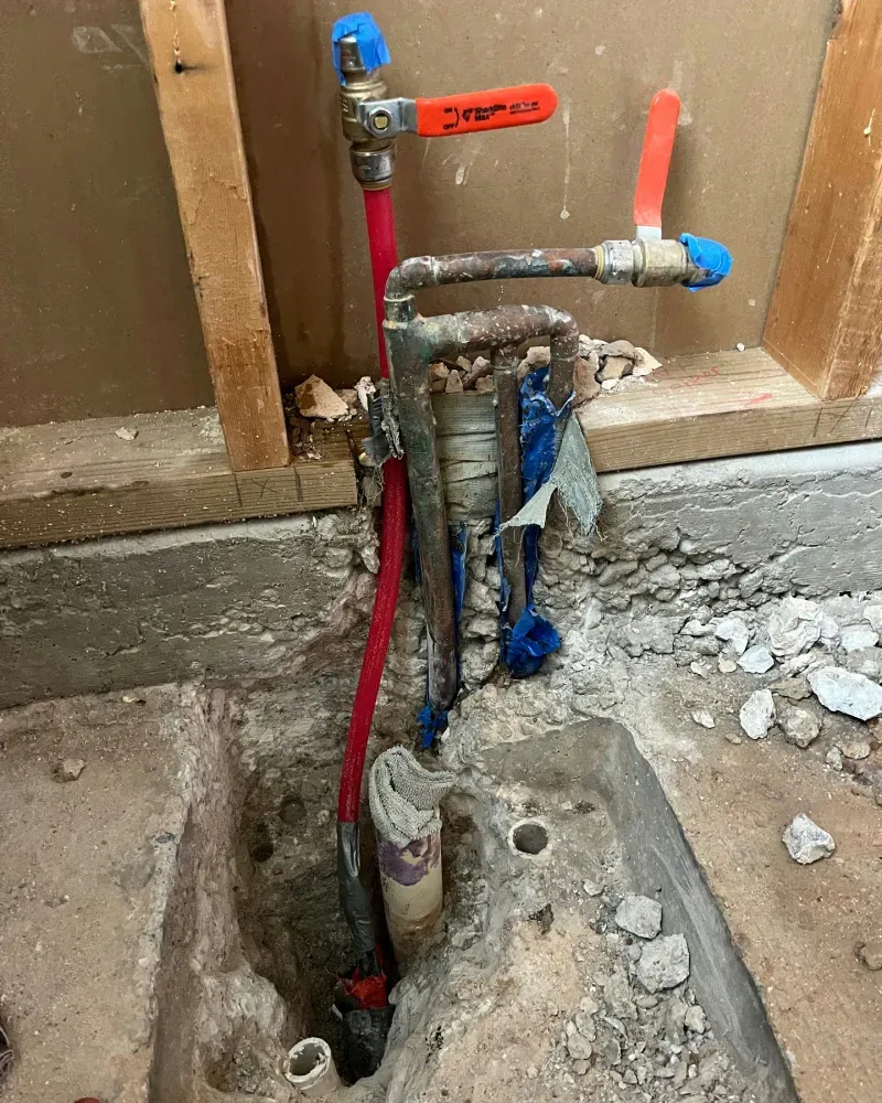 Plumbing pipes and valves in a partially demolished wall. Red and blue pipes are visible.