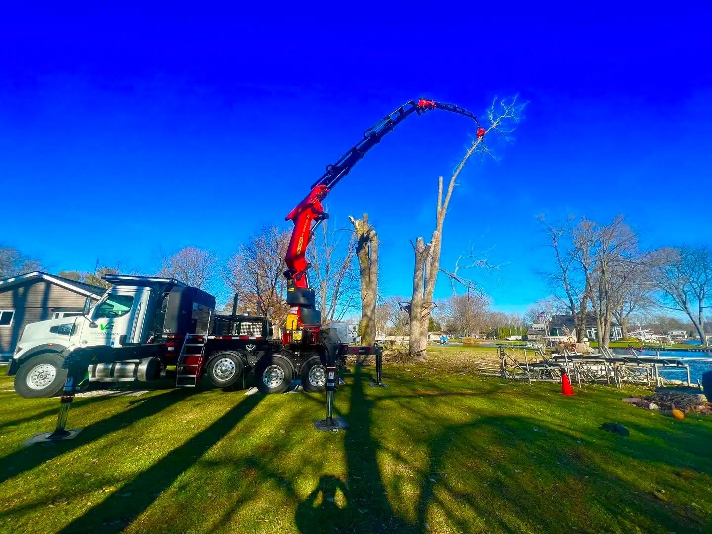 A large red crane trimming a tall tree on a sunny, green lawn.
