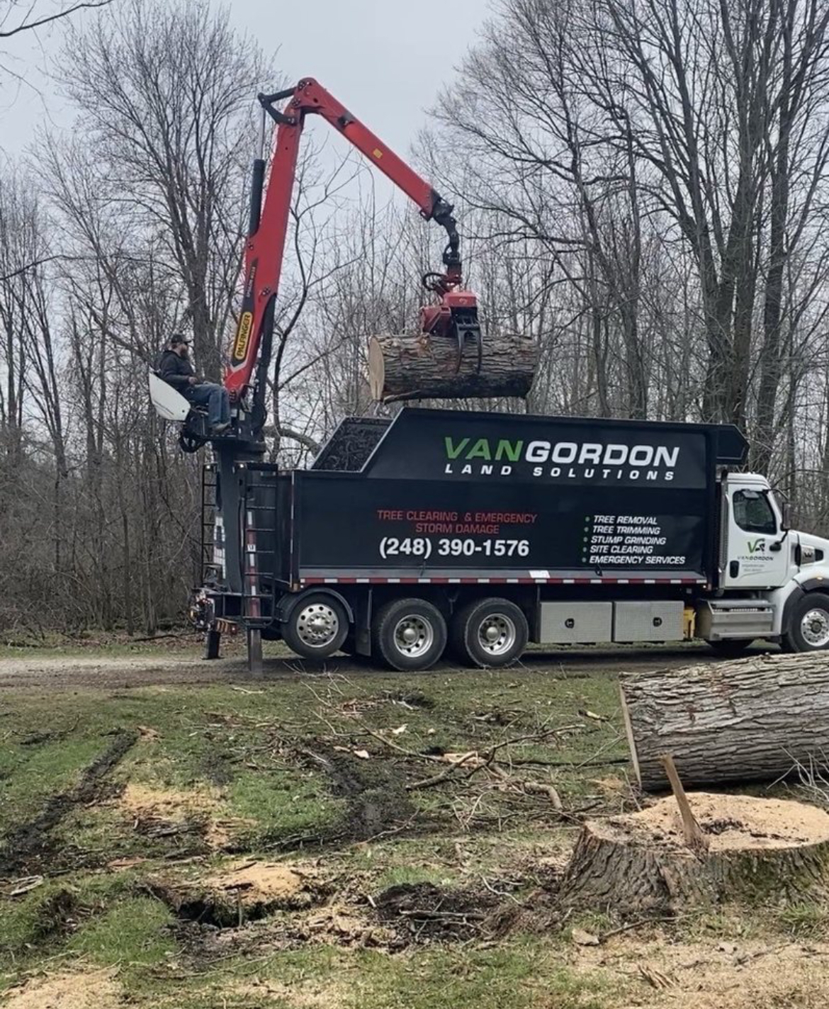 A tree service truck with a crane lifting a log into a black container.