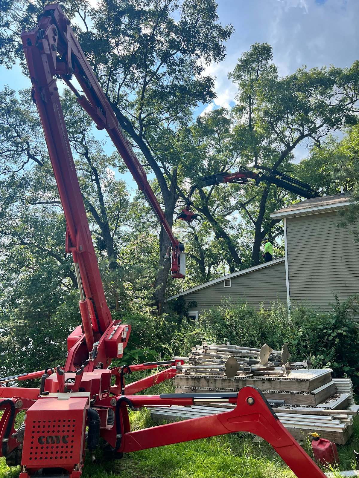Red aerial lift trimming tree branches near a house.