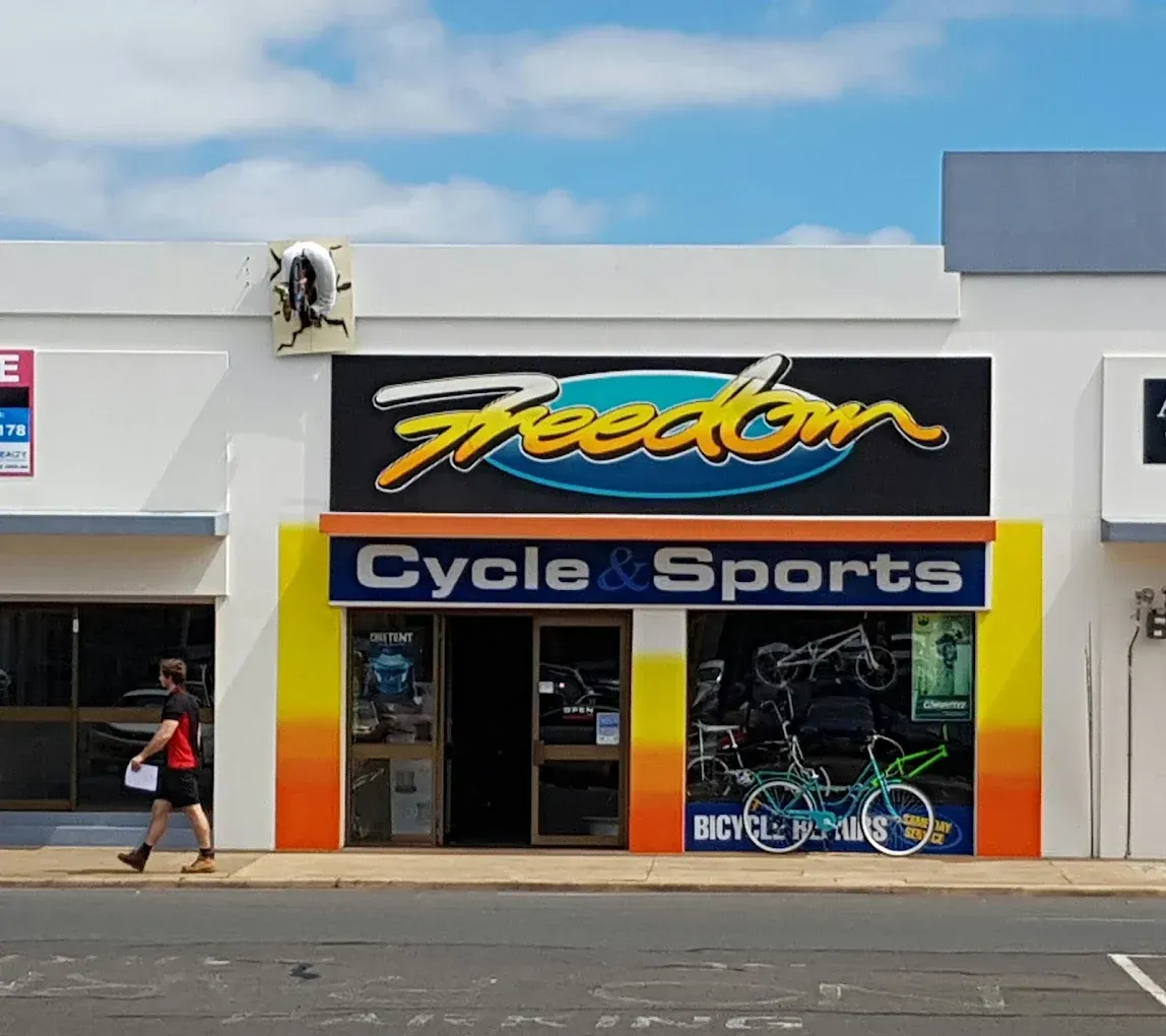 Freedom Cycle & Sports store front with a person walking by. Blue, yellow, and orange signage. — Freedom Sports in Bundaberg Central, QLD