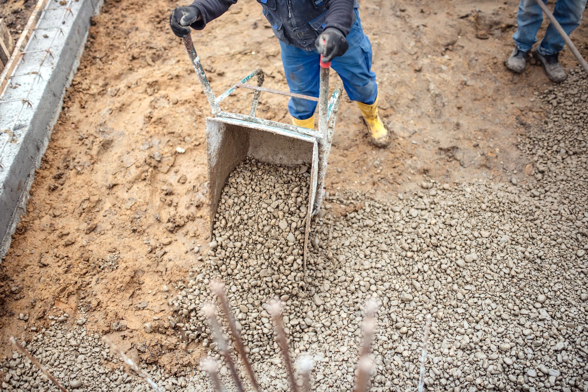 Obrero de la construcción arrojando grava desde una carretilla sobre una base preparada.