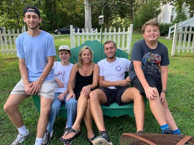 Five people sitting on a green couch outdoors in a yard, smiling at the camera.
