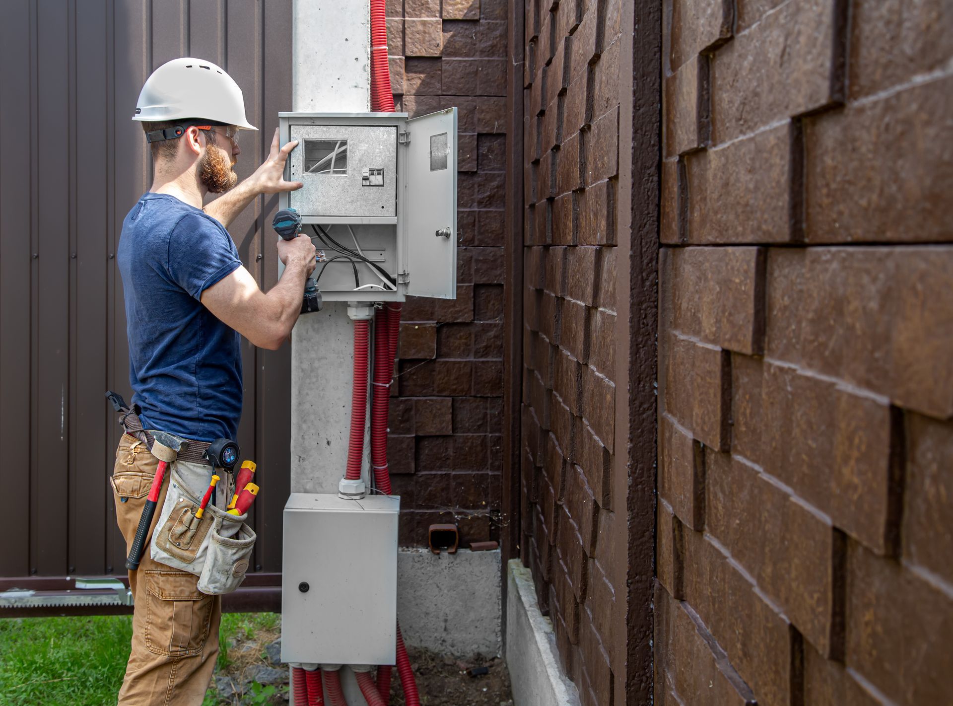 Technician in hard hat installing an outdoor electrical panel beside a brown wall