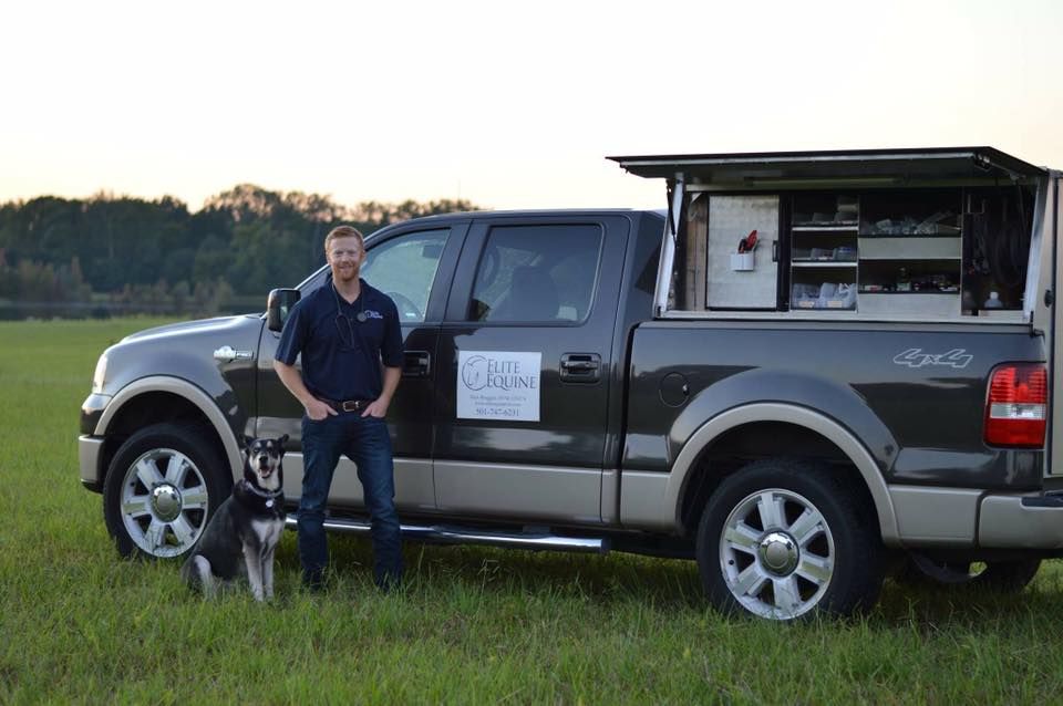 A man and a dog are standing next to a truck in a field.