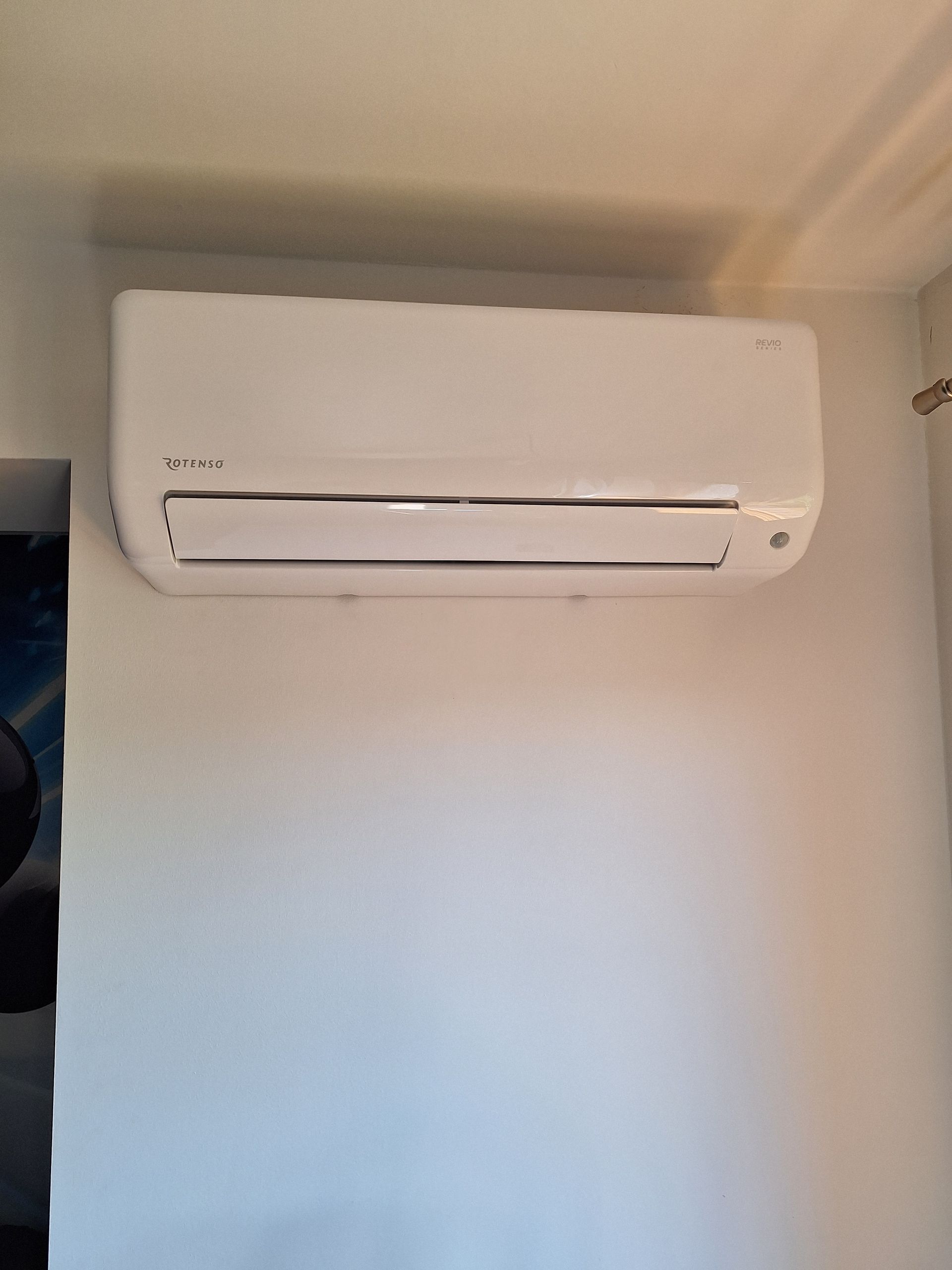 Klimatyzator ścienny Rotenso Revio w białym kolorze, o mocy 3,5 kW, zamontowany na białej ścianie w domu