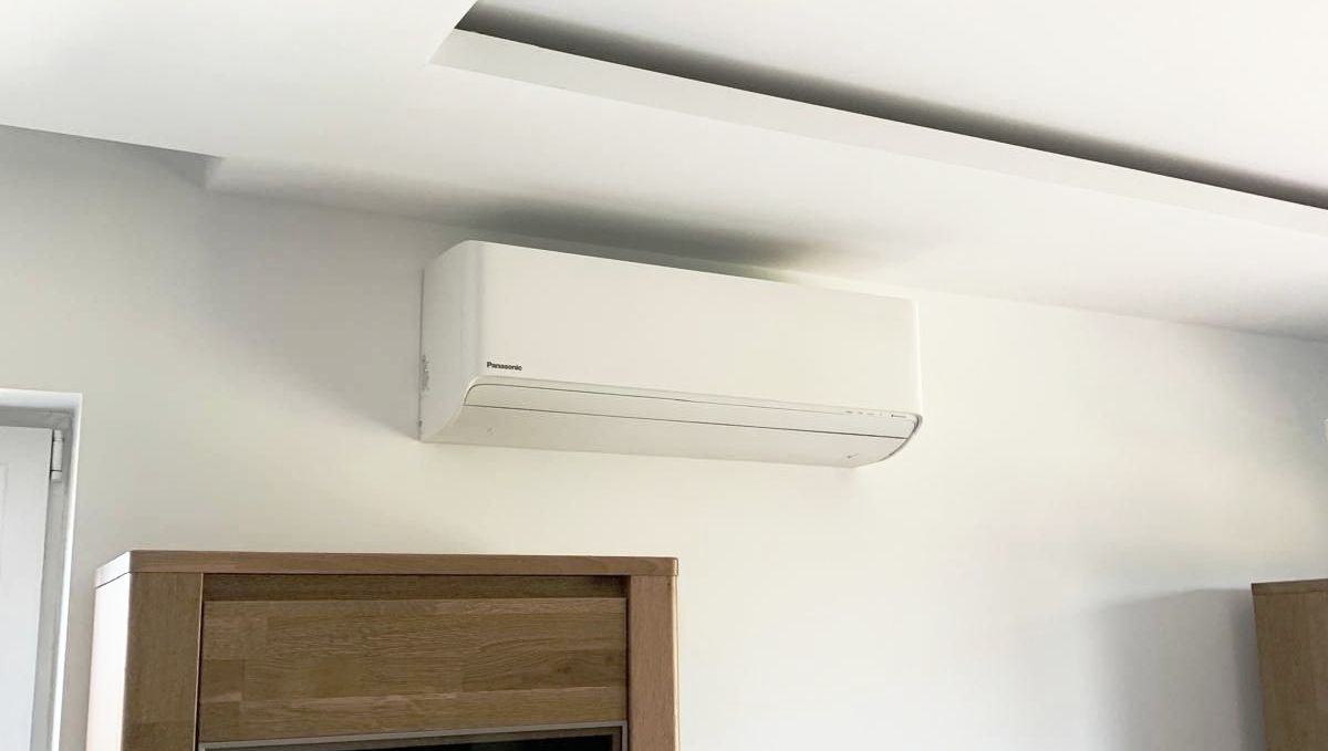Biała klimatyzacja Panasonic wisi pod sufitem w pokoju.