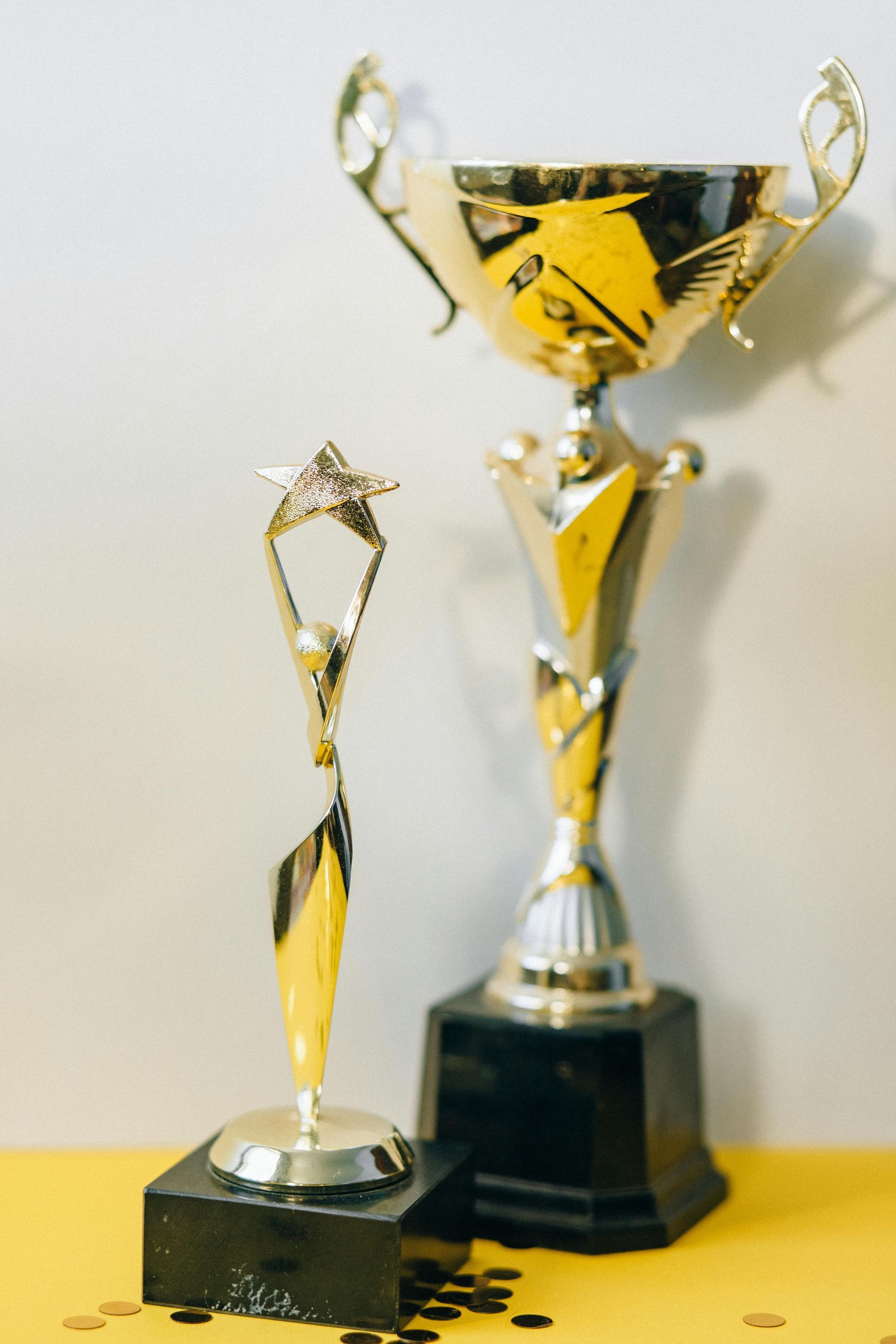 Two gold trophies are sitting on a yellow table.