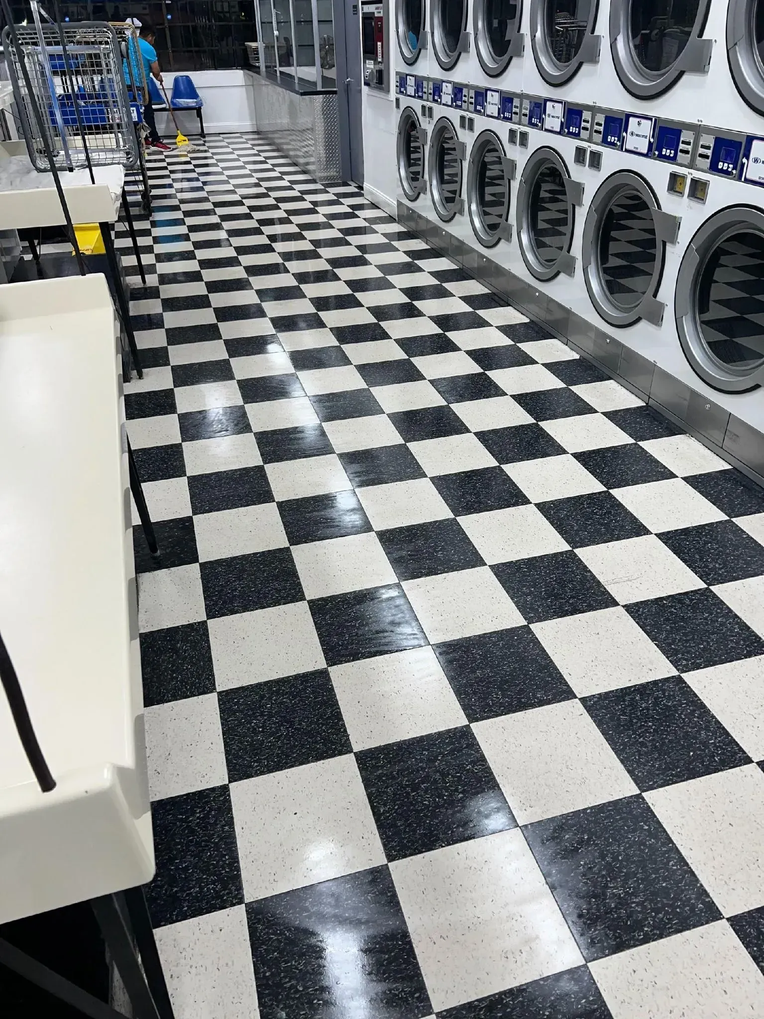 Checkerboard floor in laundromat with rows of washing machines.