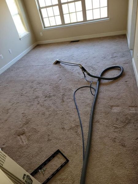 A room with light brown carpet, being cleaned with a carpet cleaning machine.