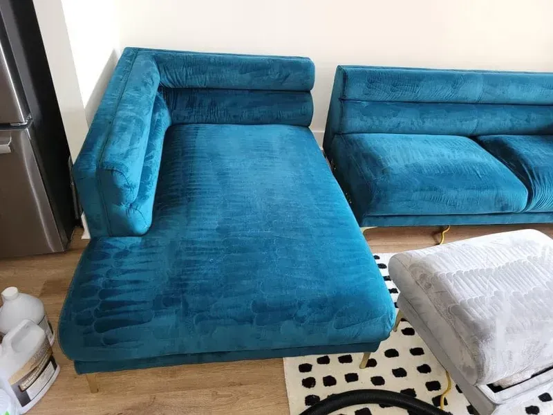 Teal-colored sectional sofa being cleaned with a carpet cleaning machine.