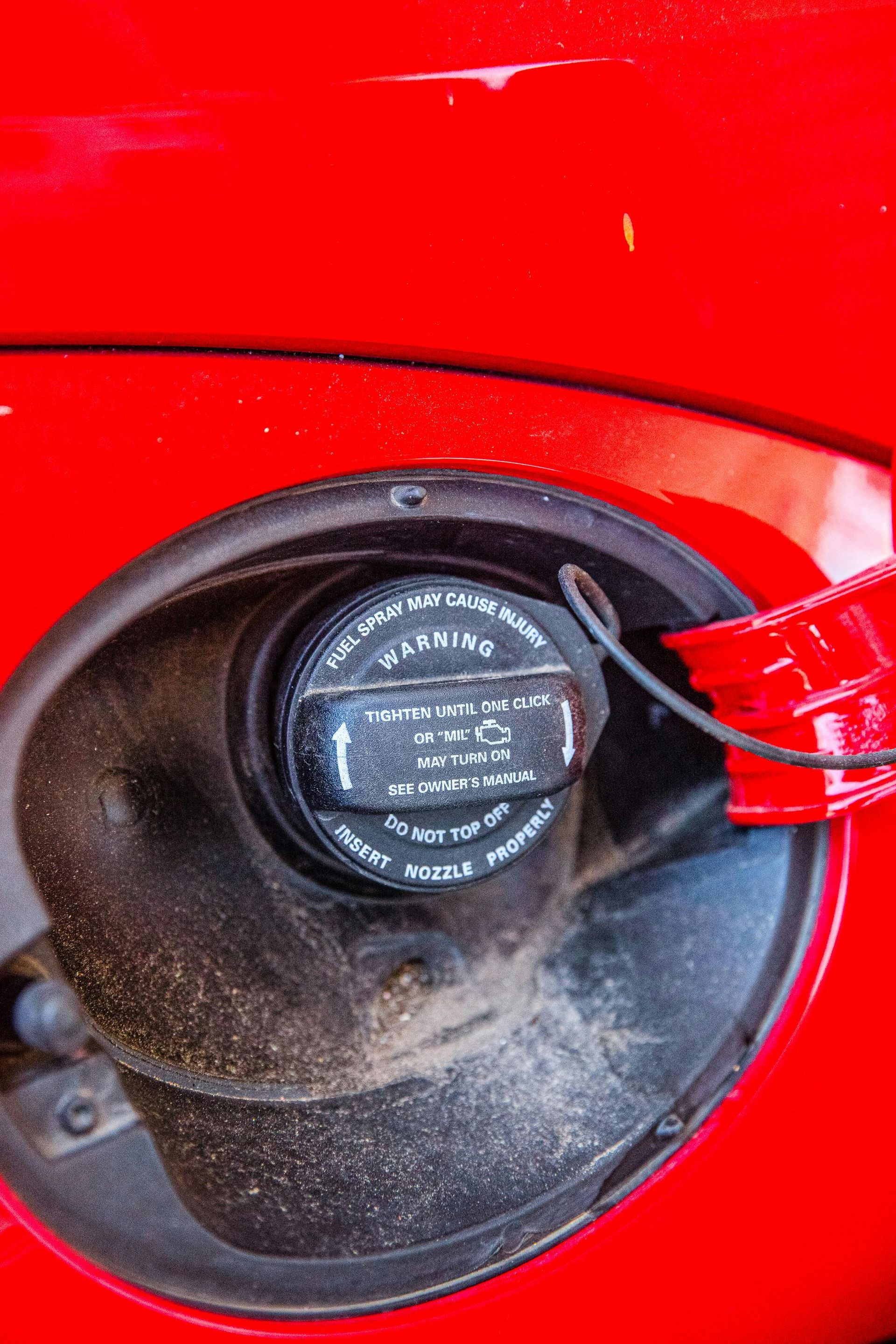 Close-up of a red car's gas tank opening with a black gas cap.