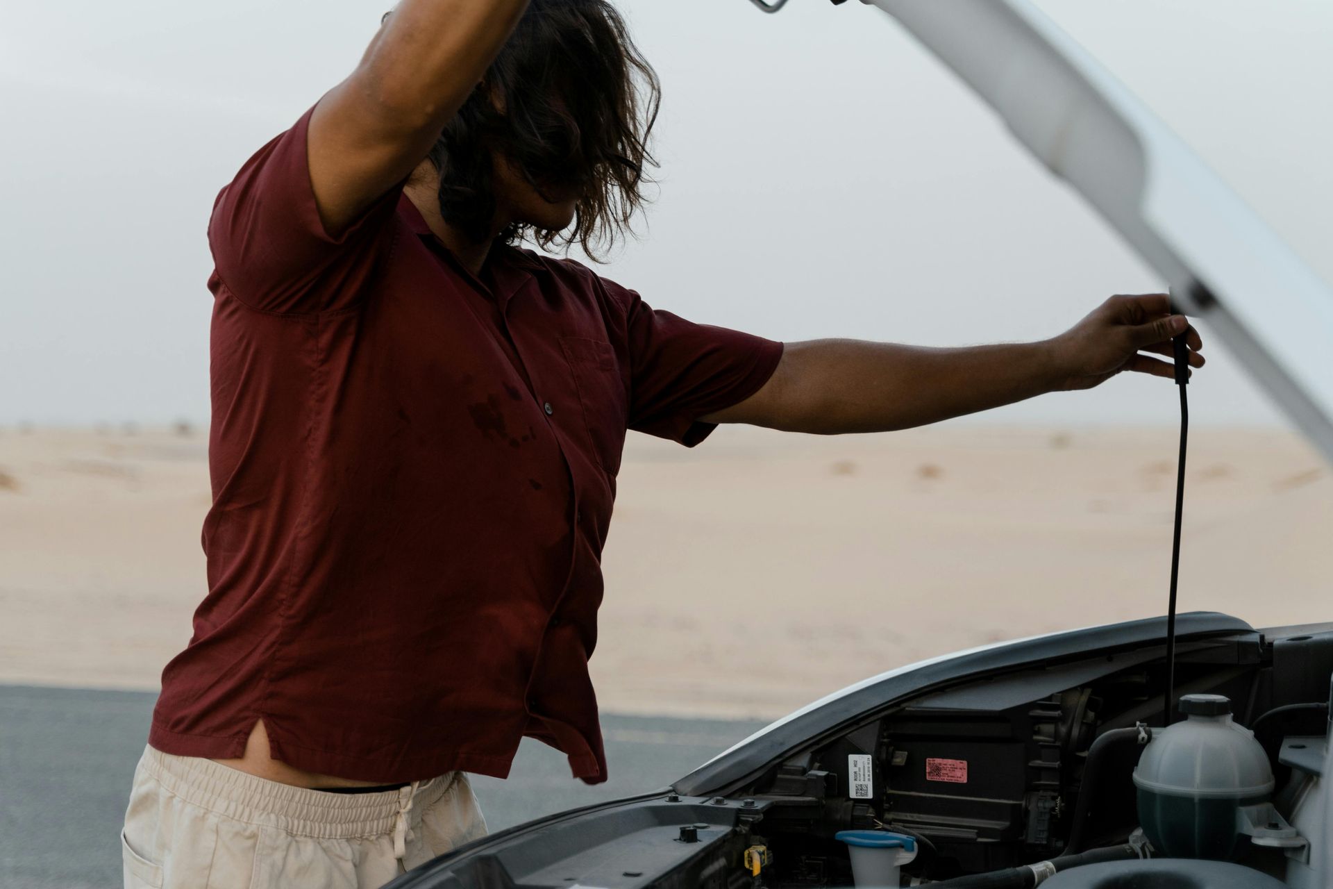 Person in red shirt checking car engine in a desert setting.