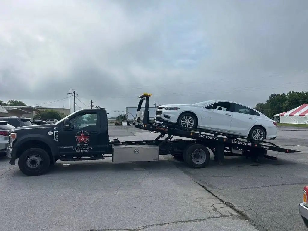 A white car is towed onto a black tow truck on an overcast day.