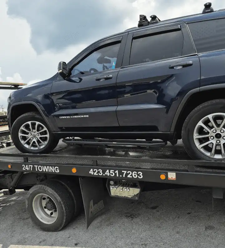 Dark blue SUV on a tow truck, parked under a cloudy sky. The tow truck has phone number 423.451.7263.