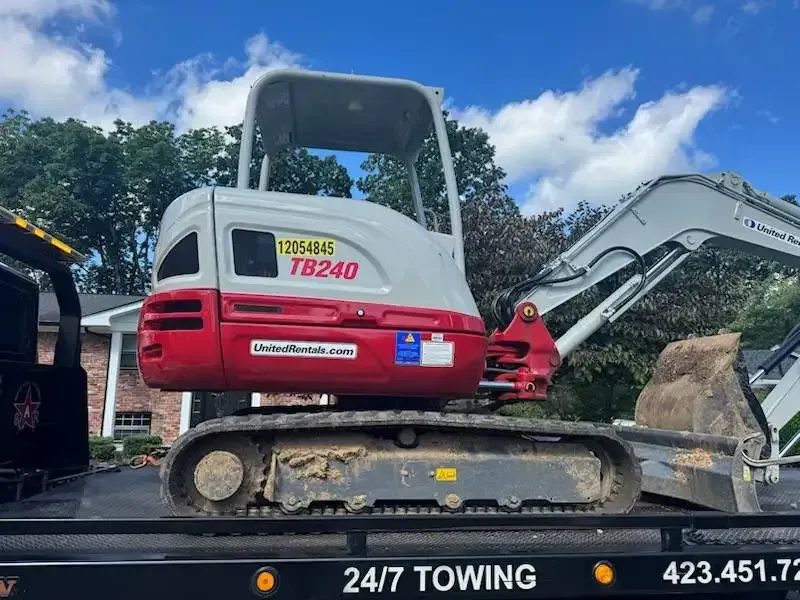 Small red and gray excavator, model TB240, on a flatbed tow truck.