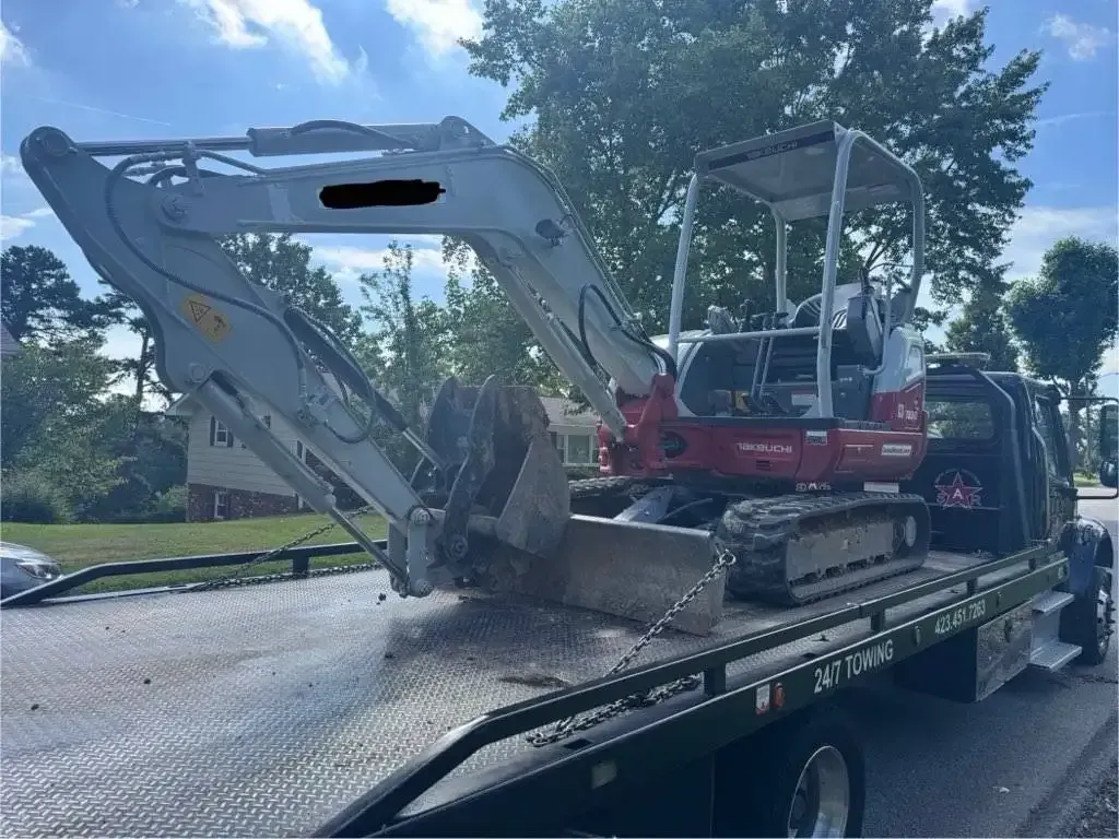 Mini excavator on a flatbed tow truck. Gray and red machine. Outdoors, daytime.