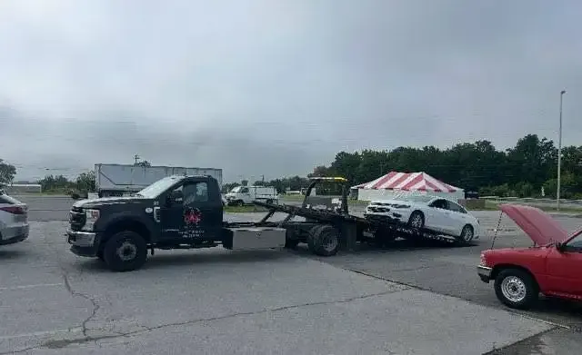 Tow truck towing a white car; scene set in an outdoor area on a cloudy day.