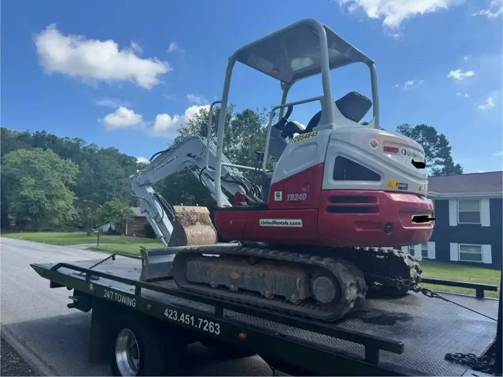 A red and white Takeuchi excavator on a black flatbed truck in a residential area.