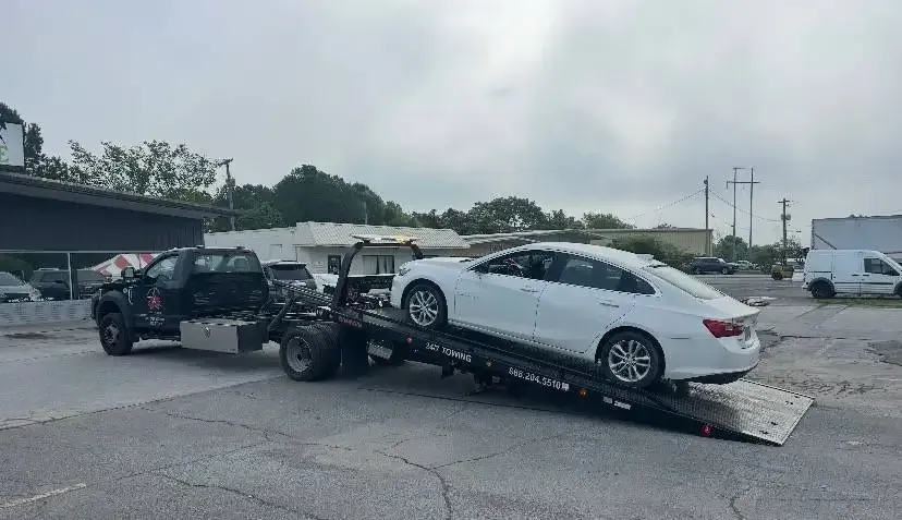 Tow truck with a white sedan on its flatbed, outdoors.