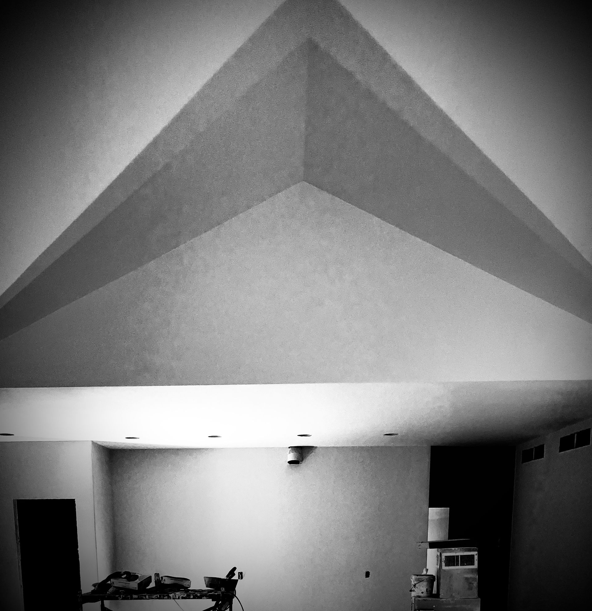 Black and white shot of a room with a triangular ceiling design; light shines down with a table and equipment below.