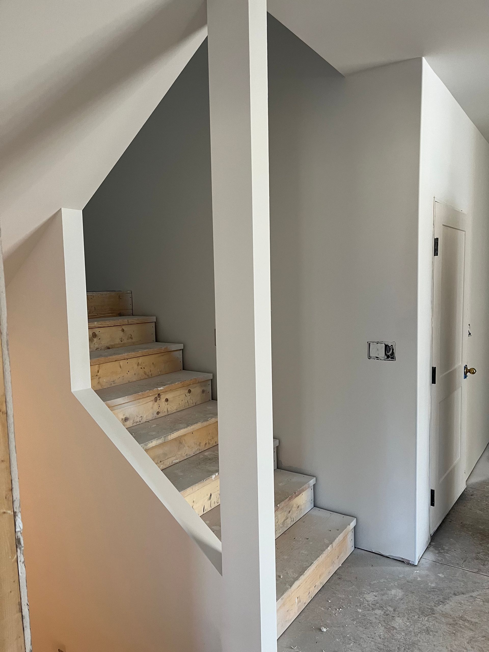 Staircase under construction with unfinished wooden steps, painted walls, and a support column.