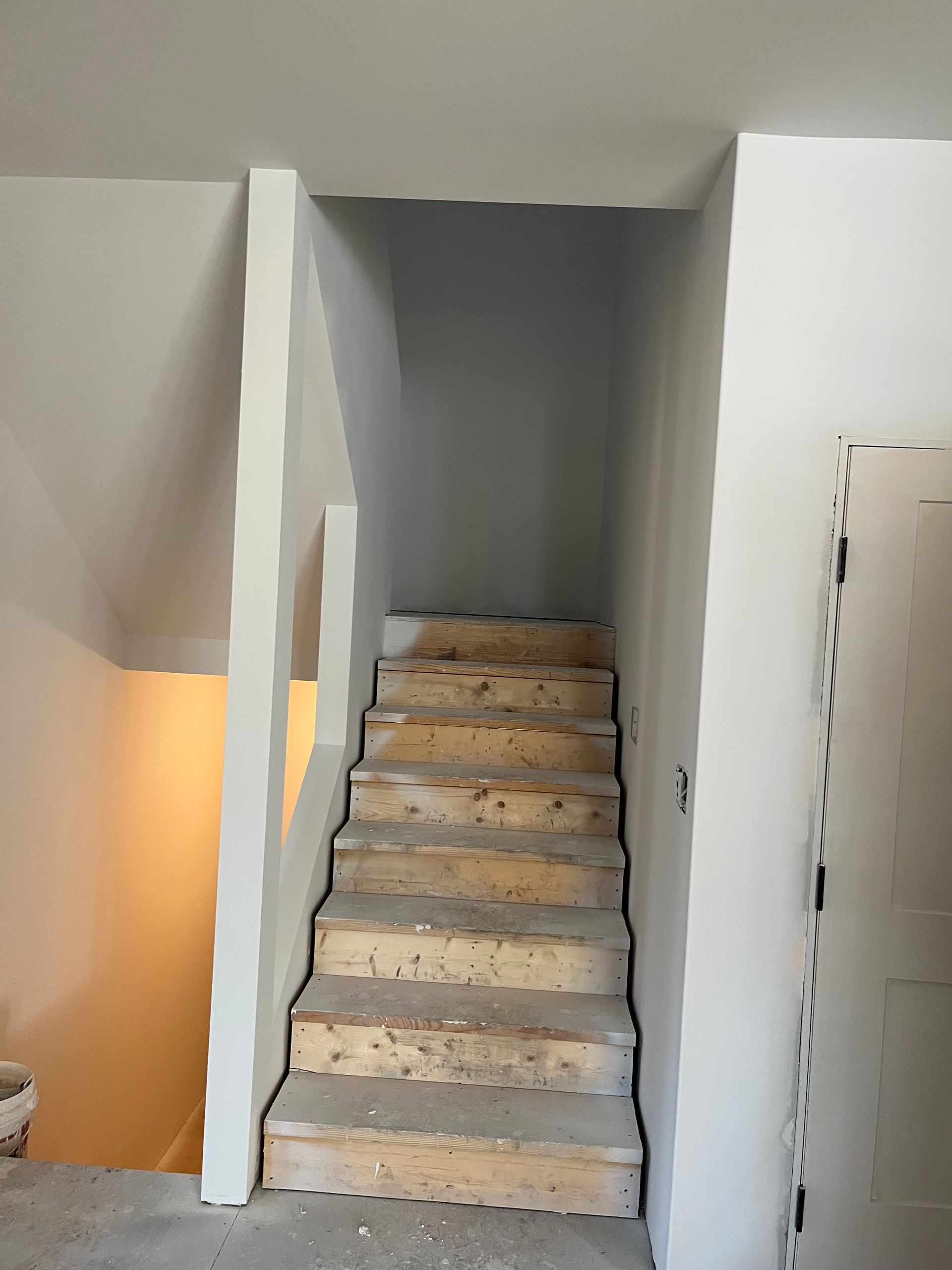 Staircase leading up, with light gray walls and unfinished wooden steps.