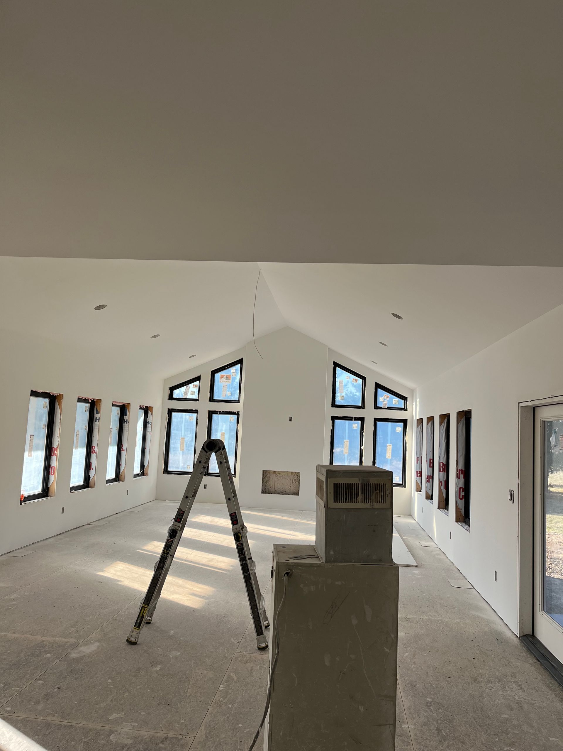 Interior of a room under construction, with many windows, a ladder, and a partially built chimney.