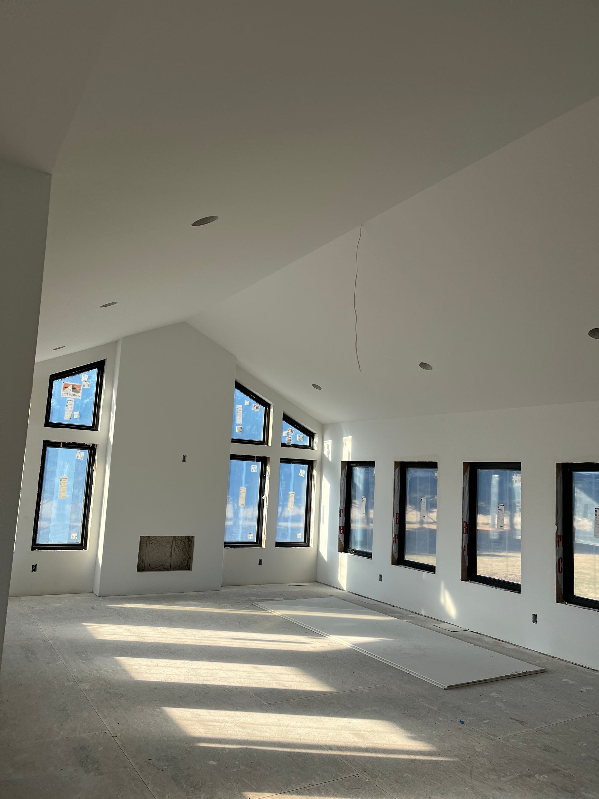 Interior of a newly constructed living room with large windows, fireplace, and unfinished flooring.