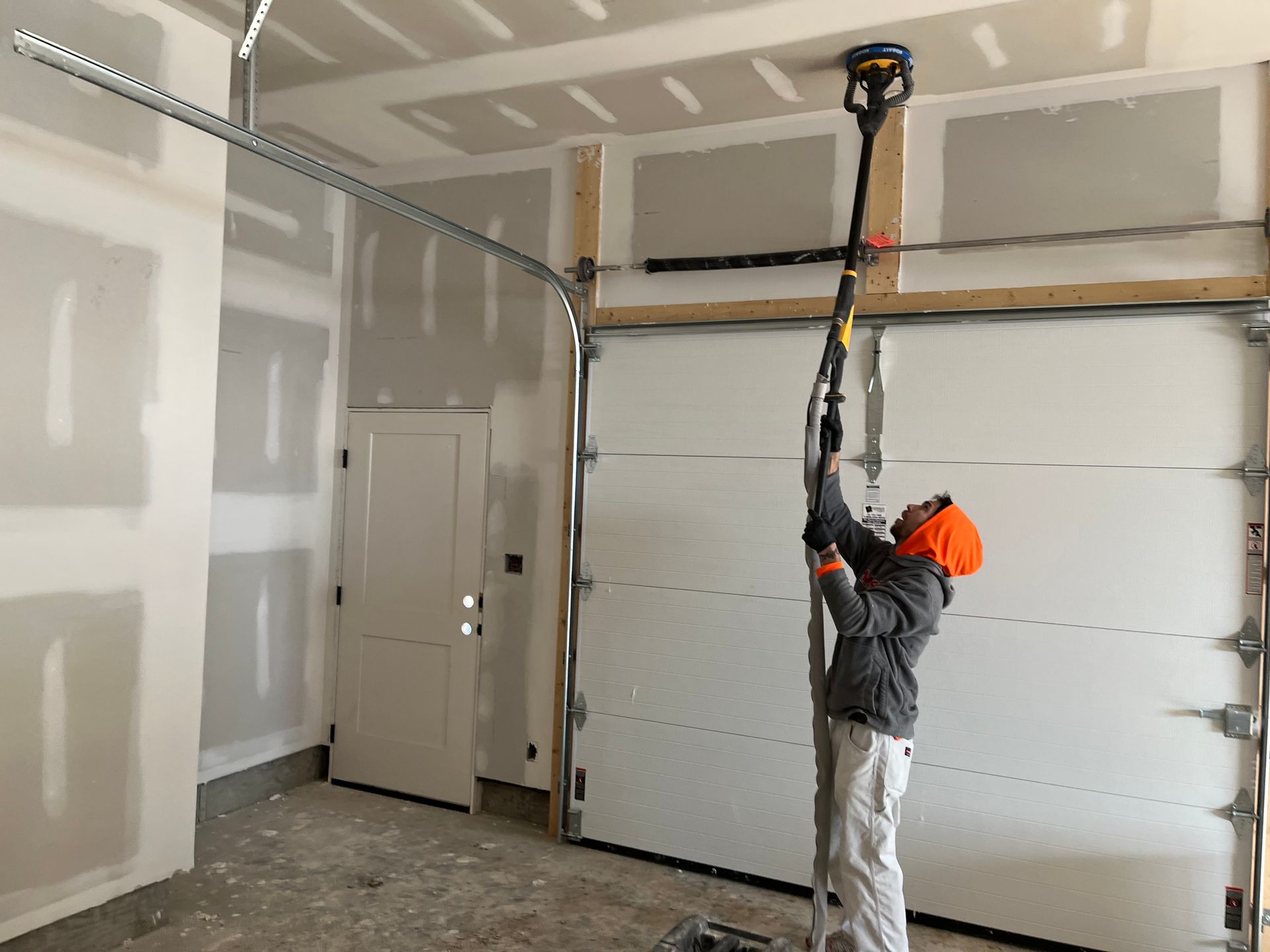 Person sanding a drywall ceiling in a garage using a pole sander.