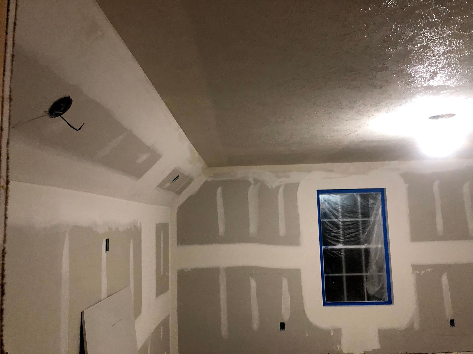 Room interior with exposed drywall and a window; the ceiling appears wet.