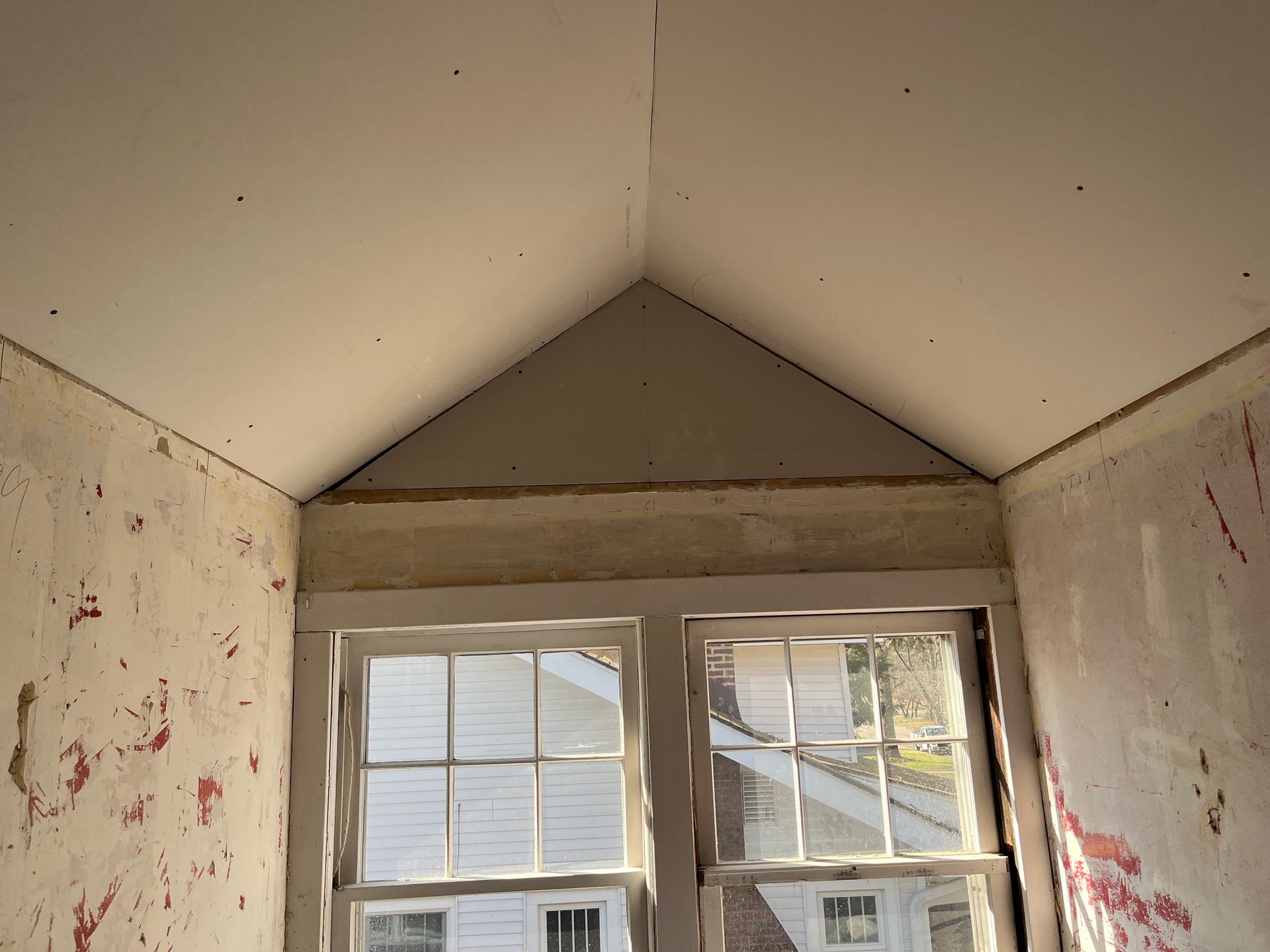 Interior view of a window alcove in a room with peeling paint and an angled ceiling. Sunlight streams through the windows.