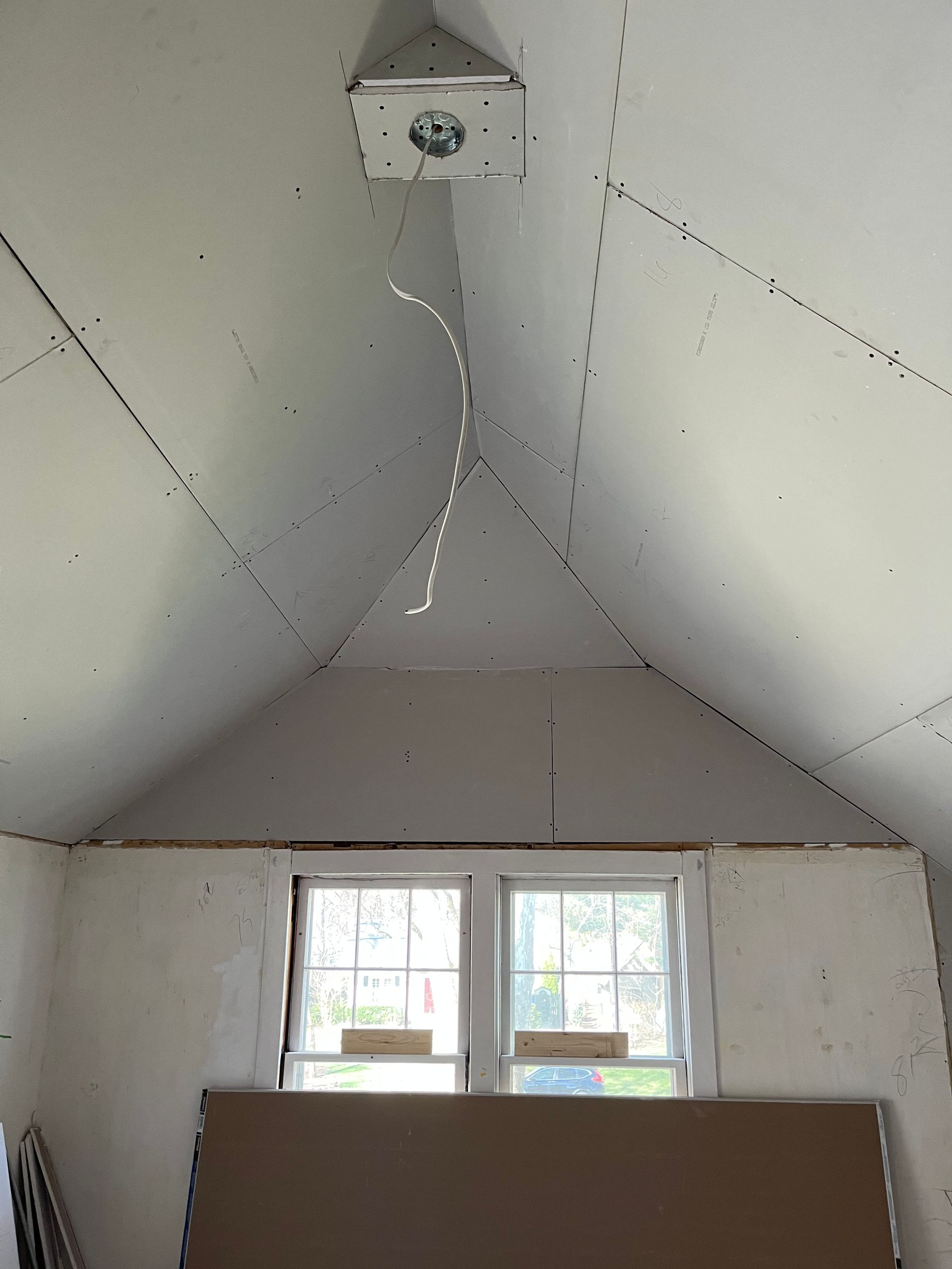 Interior view of an attic with drywall ceiling, light fixture, and two windows.