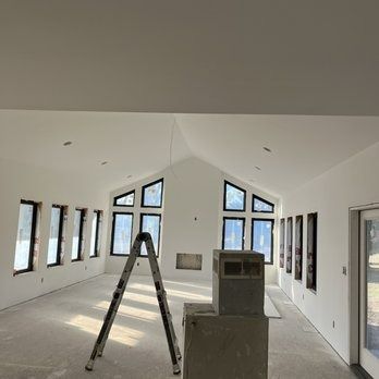 Interior of a room with white walls, black-framed windows, a ladder, and a concrete structure.