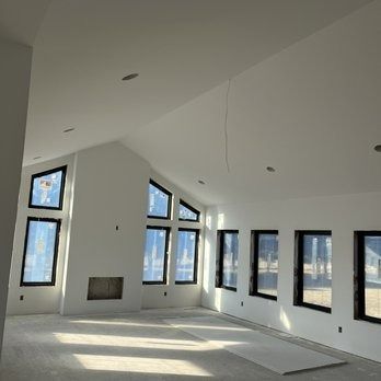 Interior of a room with large windows, fireplace, and unfinished drywall. The space is bright.