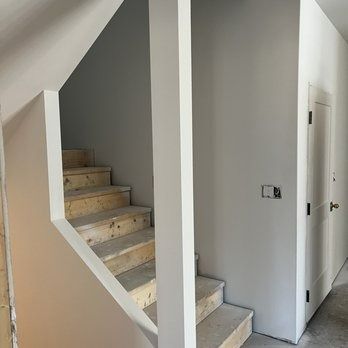 Staircase with unfinished steps and gray walls, a white column and a door.