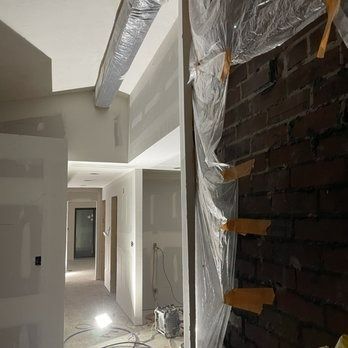 Construction worker using a drill to install drywall; interior setting, ladder.