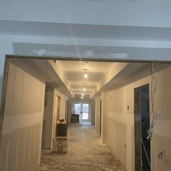 Construction of a long hallway with drywall. Lights and doorways are visible.