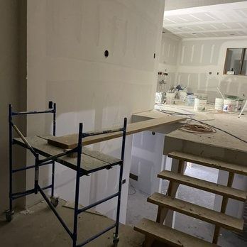 Interior construction site, drywall installed. Scaffolding, staircase, and buckets are visible.