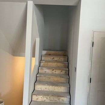 Staircase with wooden steps and a white wall to the right. The walls are painted in gray and white colors.