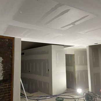 Interior construction with drywall on walls and ceiling; exposed brick, work lights, doorway.