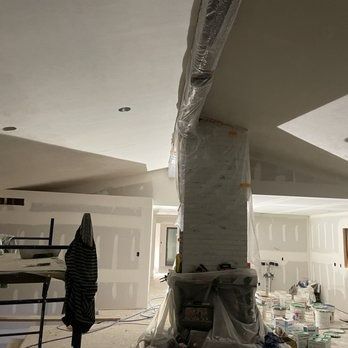 Interior construction site with exposed drywall, unfinished pillar, and plastic sheeting.