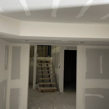 Interior view of a room under construction with exposed drywall and a staircase leading down.